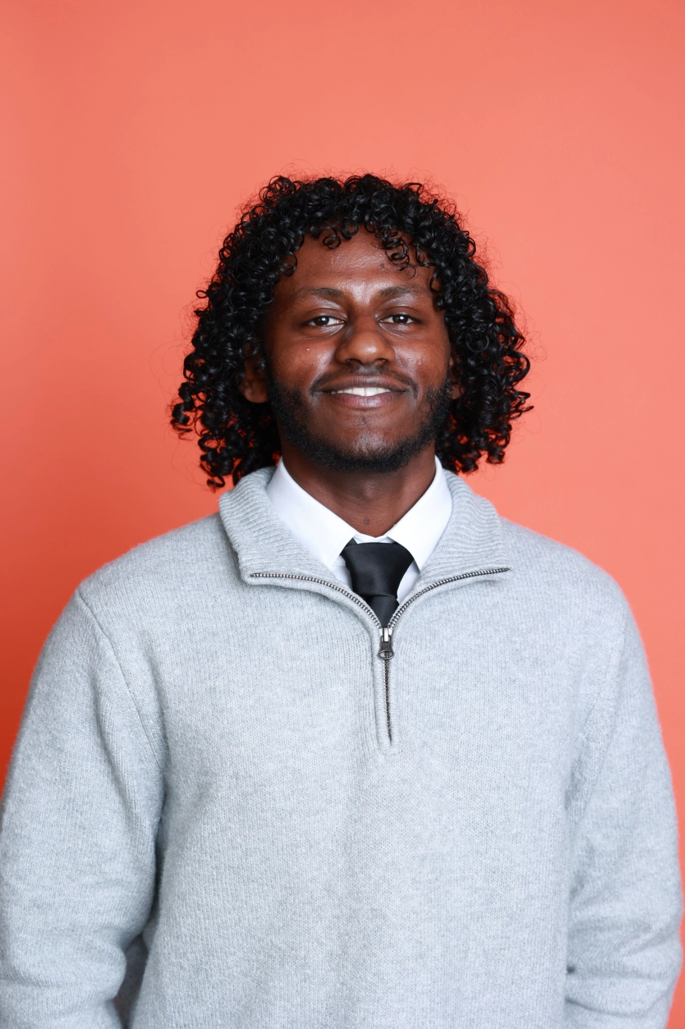 Ramzi Burhan smiling, wearing a grey sweater over a shirt and tie